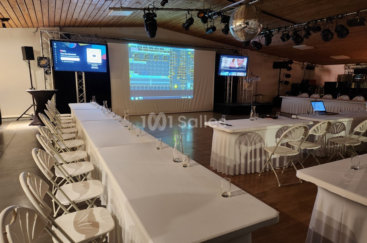 Salle de conférence avec tables, chaises, écrans de présentation et projecteur affichant des graphiques.