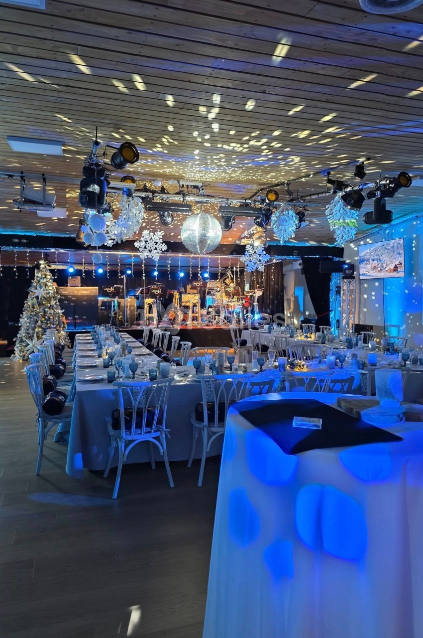 Salle de réception décorée pour une fête, avec tables dressées, scène éclairée et sapin de Noël illuminé.