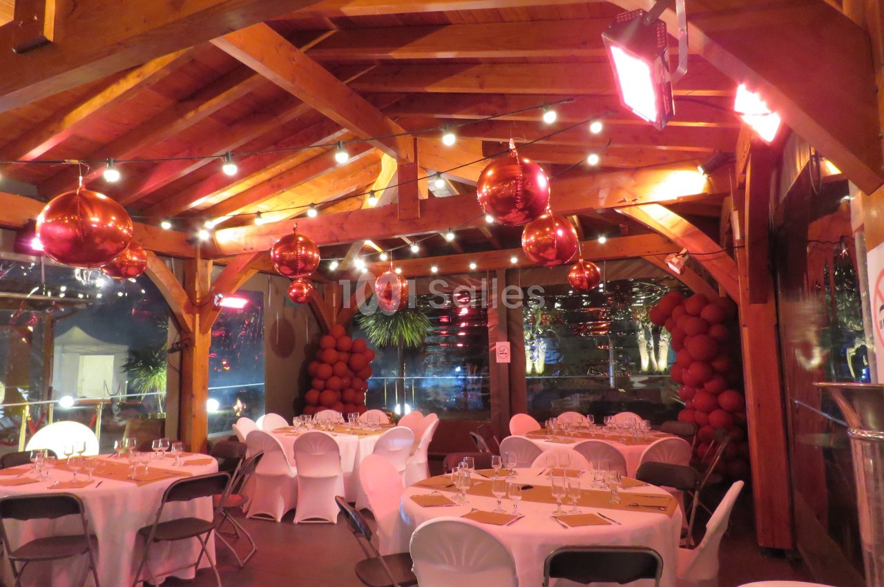 Salle décorée avec des guirlandes lumineuses, des suspensions rouges et des tables dressées pour un événement.