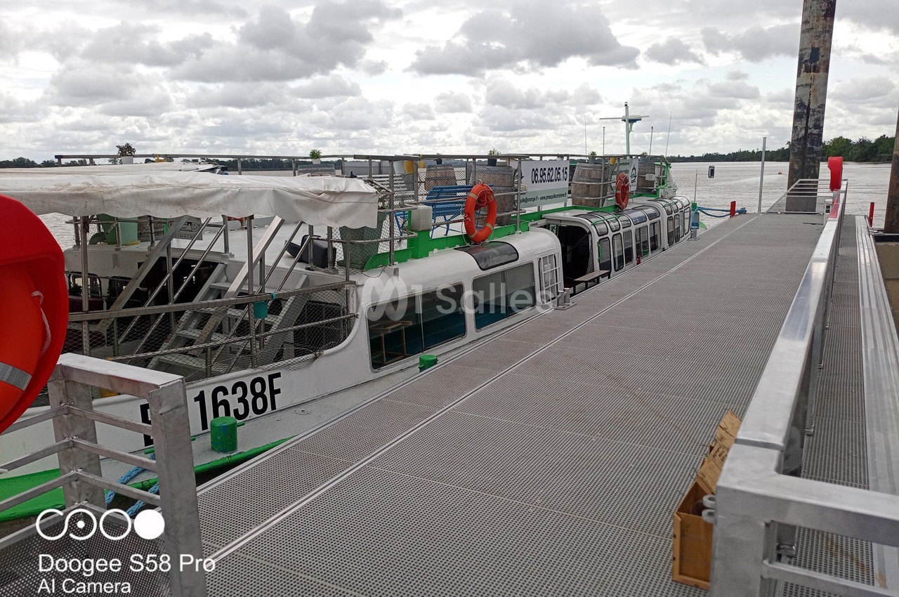Bateau amarré à un quai métallique, avec des bouées rouges et un ciel nuageux en arrière-plan.