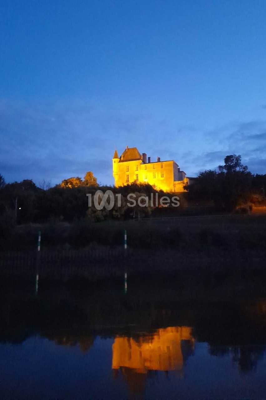 Château illuminé au sommet d'une colline, reflété dans l'eau calme au crépuscule.