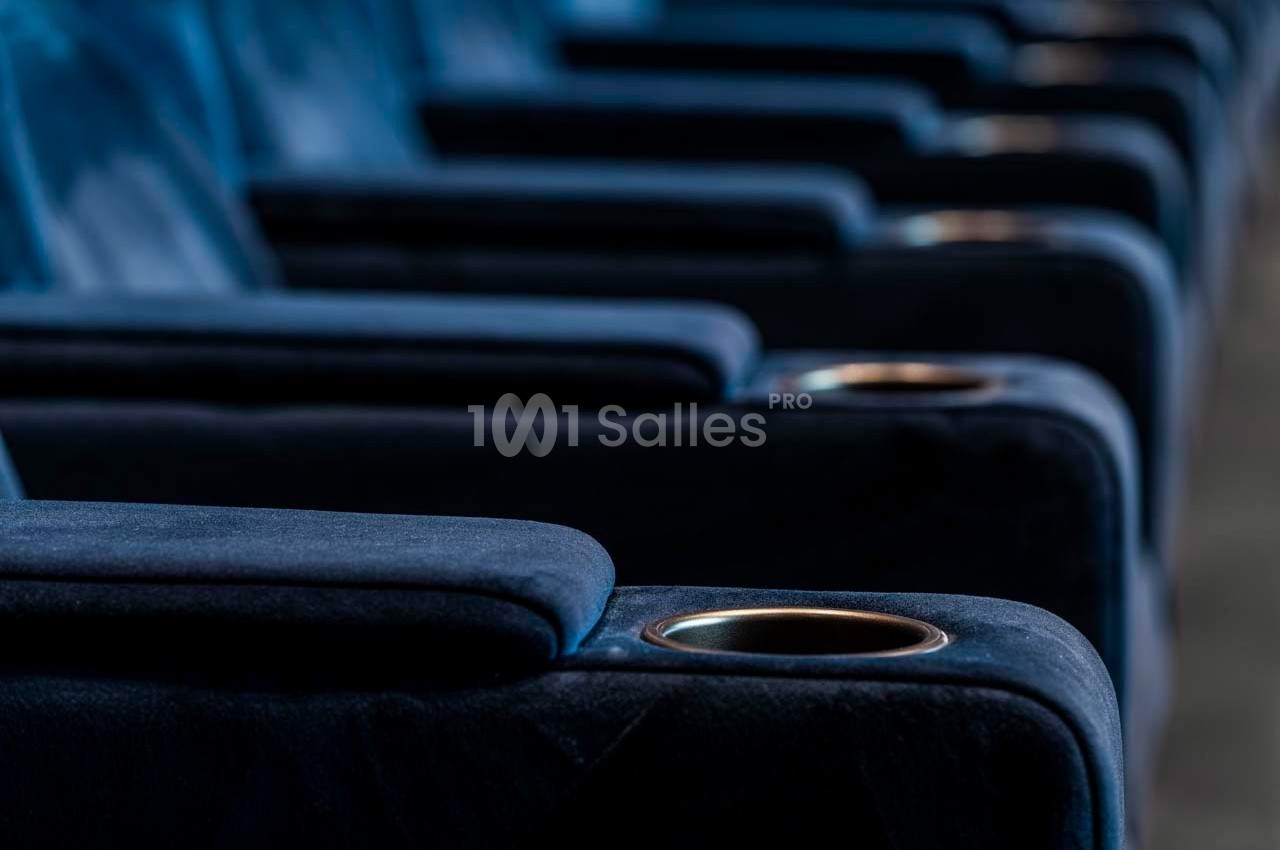 Rangée de sièges de cinéma en velours bleu avec accoudoirs et porte-gobelets intégrés.