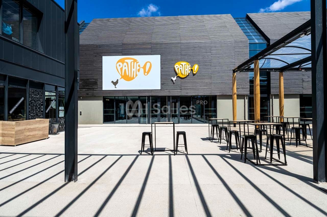 Façade d'un cinéma moderne avec terrasse extérieure équipée de tables hautes et tabourets.