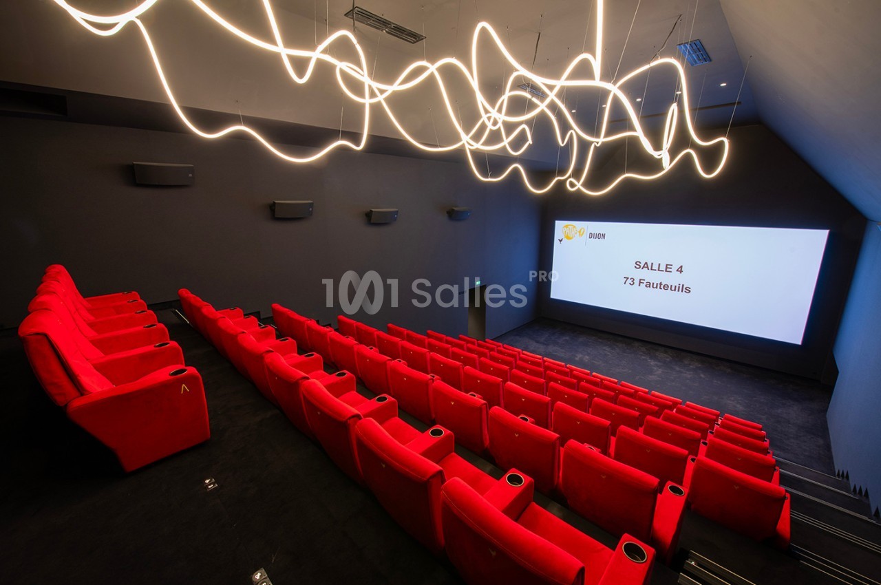 Salle de cinéma moderne avec des rangées de fauteuils rouges, un écran blanc et des éclairages design au plafond.