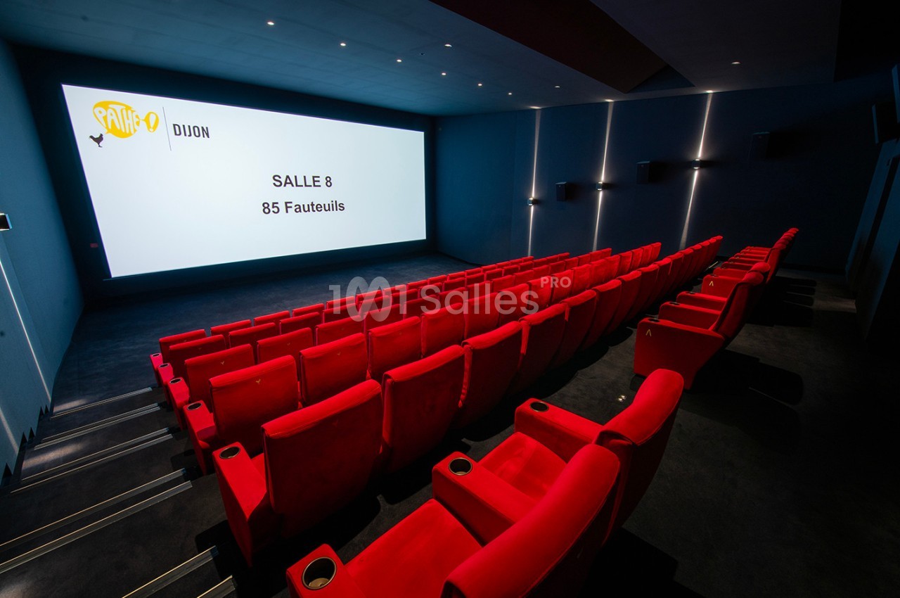 Salle de cinéma moderne avec des rangées de fauteuils rouges et un écran affichant ’Salle 8, 85 fauteuils’.