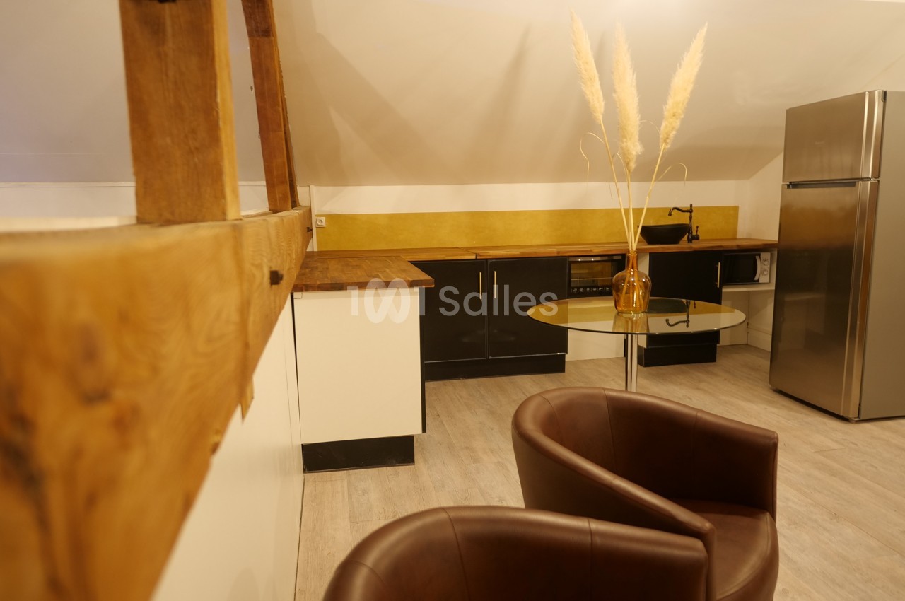 Cuisine mansardée avec comptoirs en bois, meubles noirs et blancs, table ronde, chaises en cuir et décoration minimaliste.