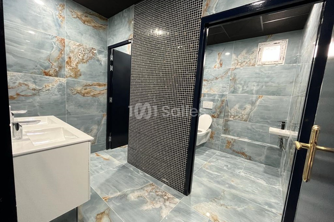 Salle de bain moderne avec carrelage effet marbre bleu, lavabo double, cabine de toilette et mur en mosaïque noire.