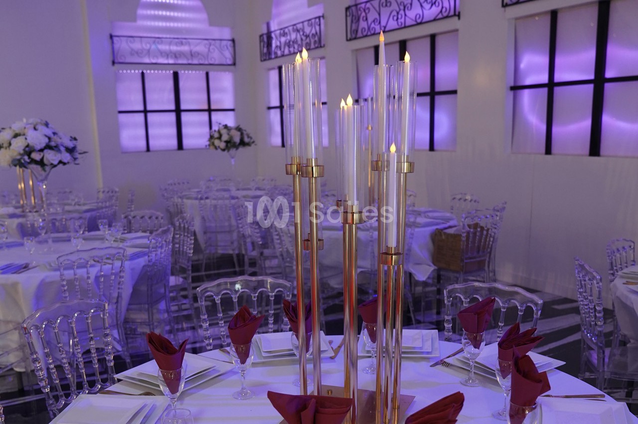 Salle de réception élégante avec tables dressées, chandeliers dorés et éclairage violet tamisé.