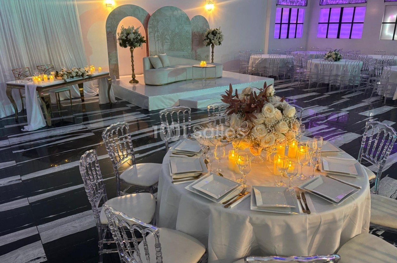 Salle de réception élégante avec tables décorées de fleurs blanches et bougies, éclairage tamisé et ambiance raffinée.