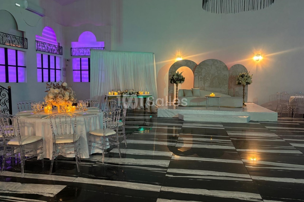 Salle de réception élégante avec tables décorées, éclairage tamisé et espace lounge sur une estrade.