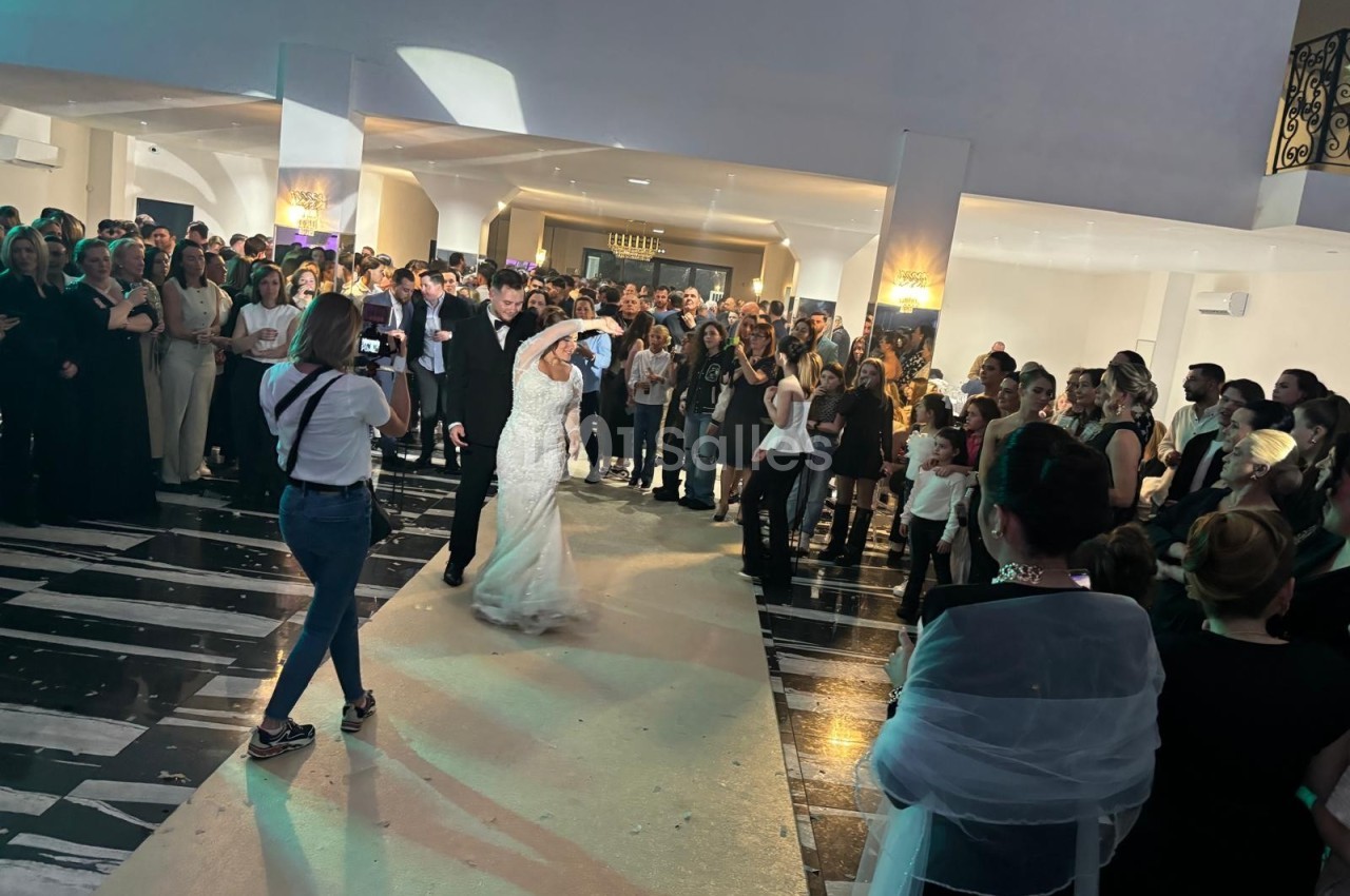 Un couple danse au centre d'une salle entourée d'invités, sous un éclairage tamisé.
