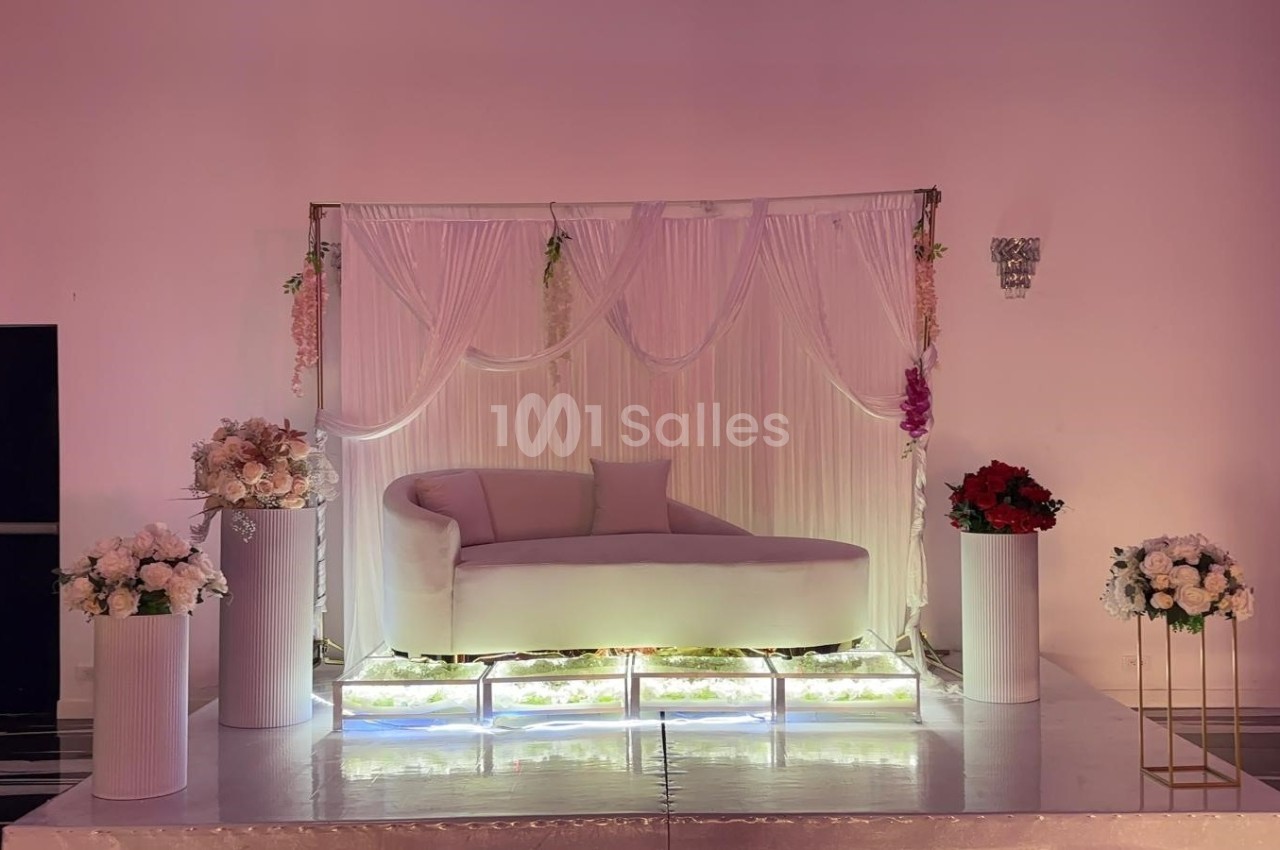 Canapé blanc décoré avec des rideaux drapés, fleurs suspendues et arrangements floraux sur des colonnes blanches.