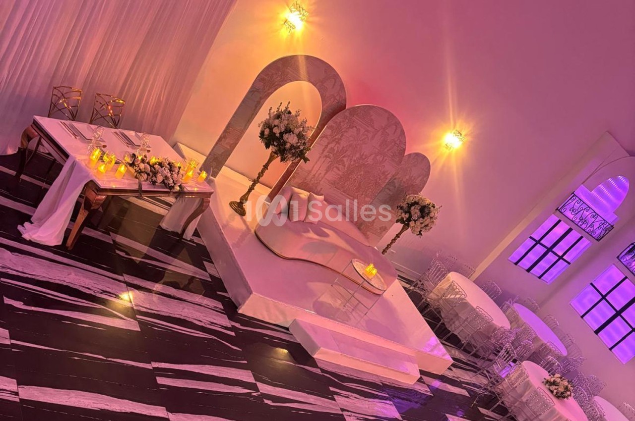 Salle de réception décorée avec une scène élégante, des tables ornées de fleurs et un éclairage violet tamisé.