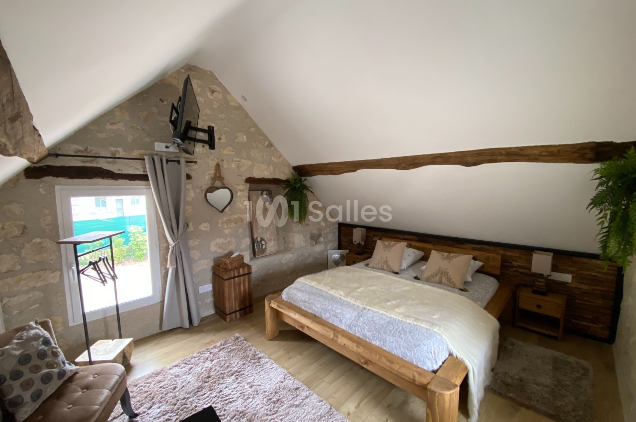 Chambre mansardée avec lit double en bois, murs en pierre, poutres apparentes et décoration naturelle.