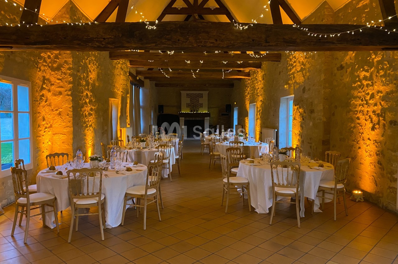Salle de réception en pierre avec tables dressées, chaises en bois et éclairage chaleureux.
