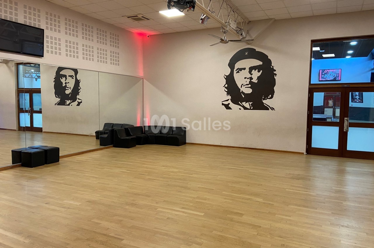 Salle de danse avec parquet clair, miroirs, sièges noirs et un portrait mural de Che Guevara.