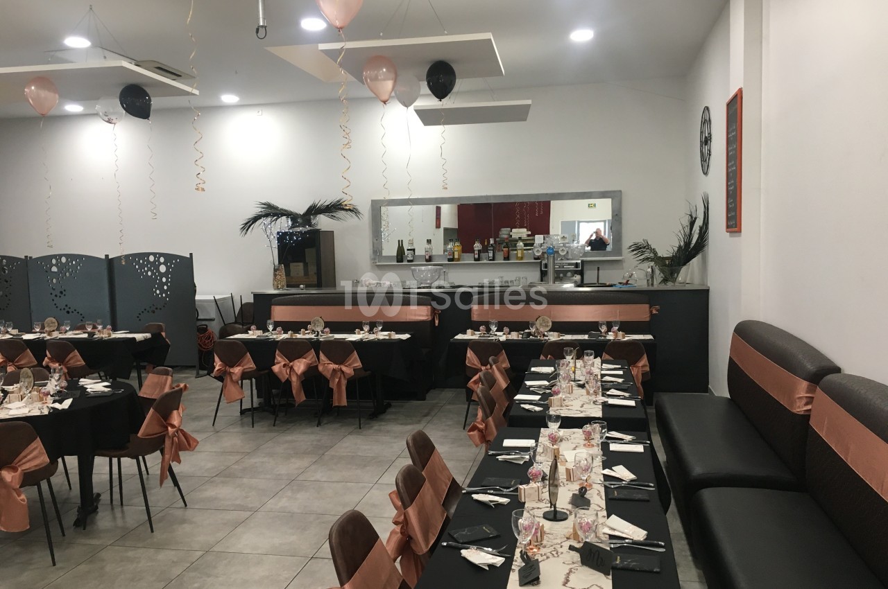 Salle de réception décorée avec des tables dressées, nappes noires et rubans roses, prête pour un événement.