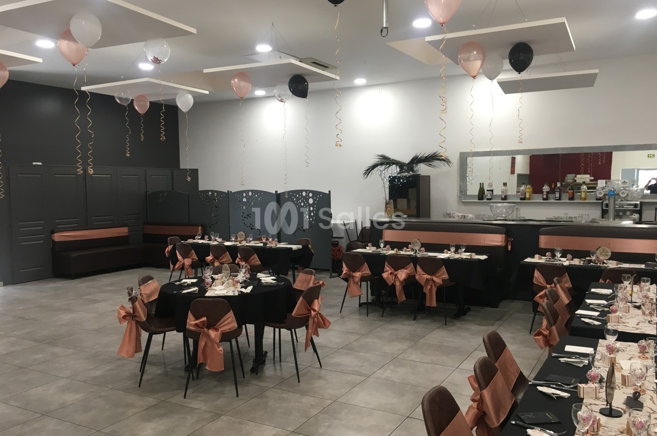 Salle de réception décorée avec des ballons noirs et roses, tables dressées avec nappes noires et nœuds roses.