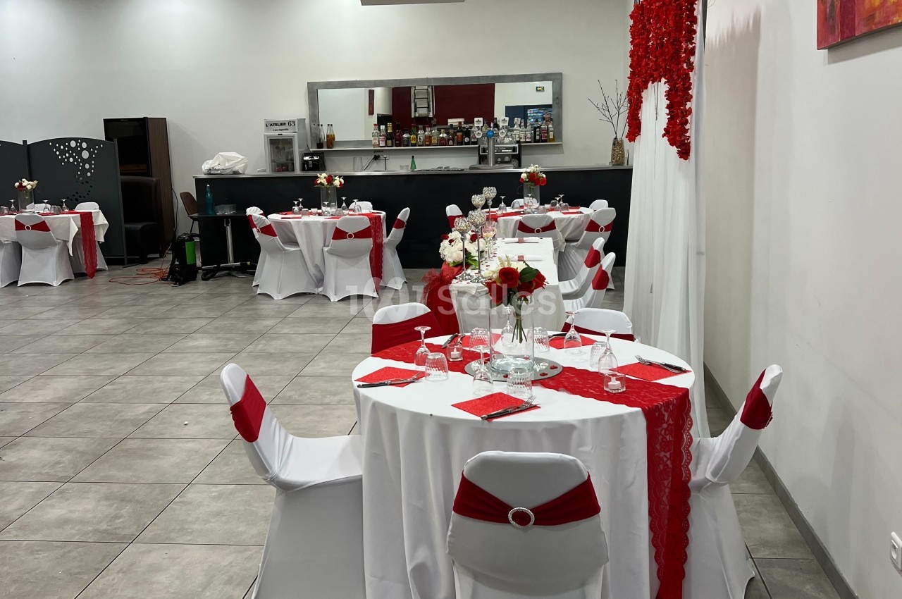 Salle de réception décorée en rouge et blanc avec tables dressées, nappes blanches et chemins de table rouges.