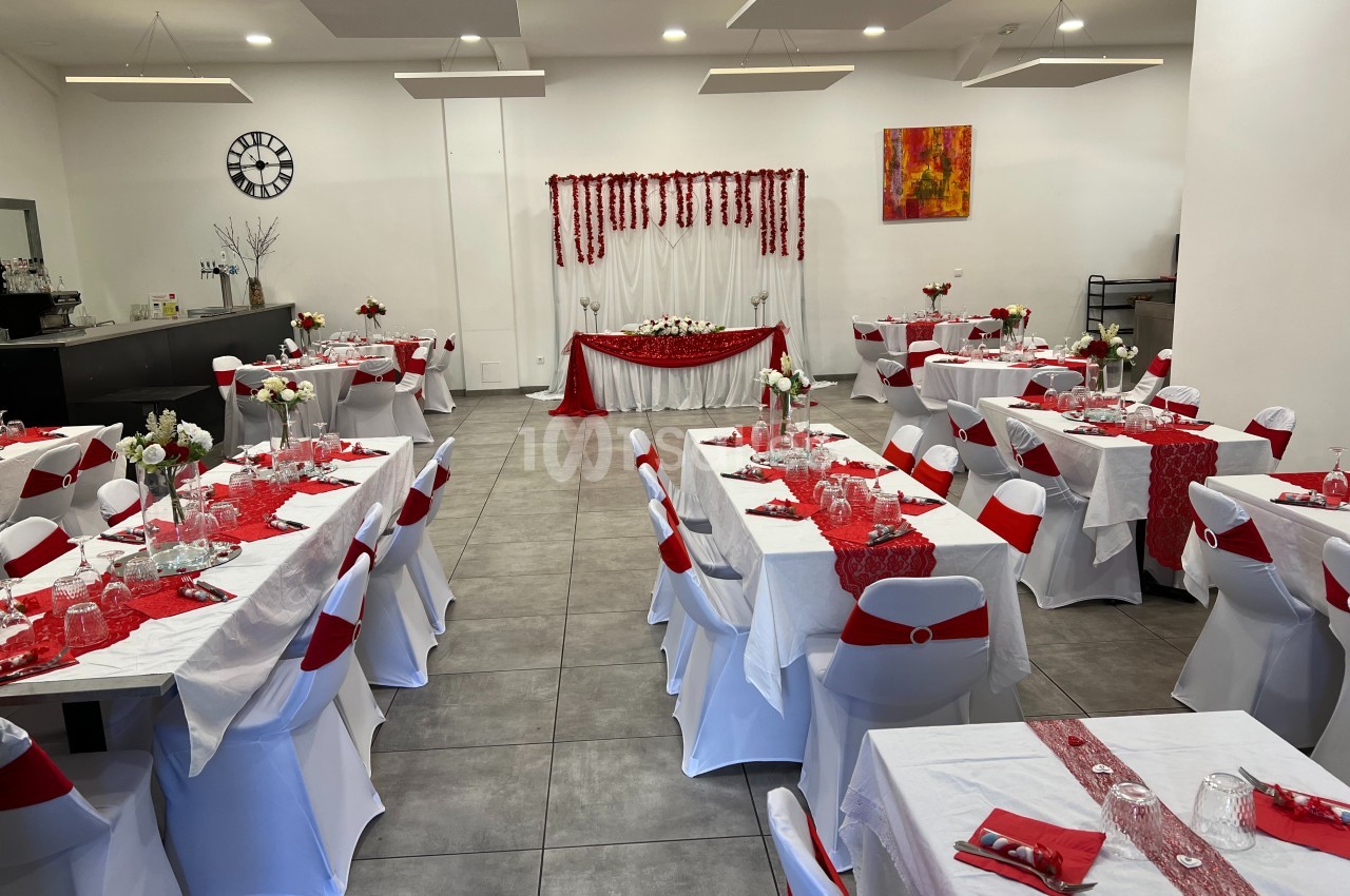 Salle de réception décorée en rouge et blanc avec des tables dressées pour un événement festif.