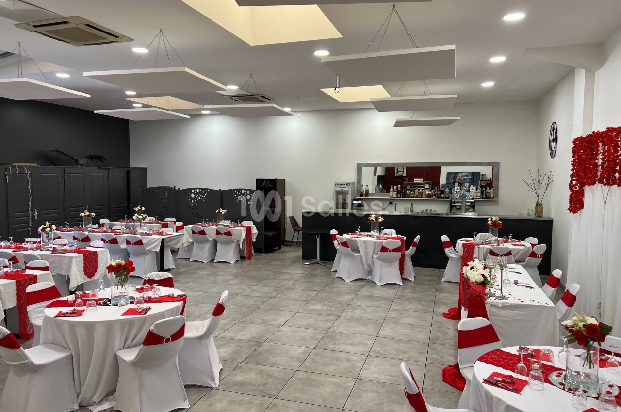 Salle de réception décorée en rouge et blanc, avec tables dressées et un bar en arrière-plan.
