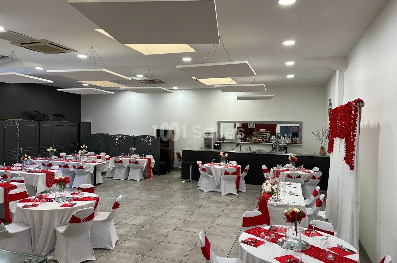 Salle de réception décorée avec des nappes blanches et rouges, tables dressées et éclairage moderne au plafond.