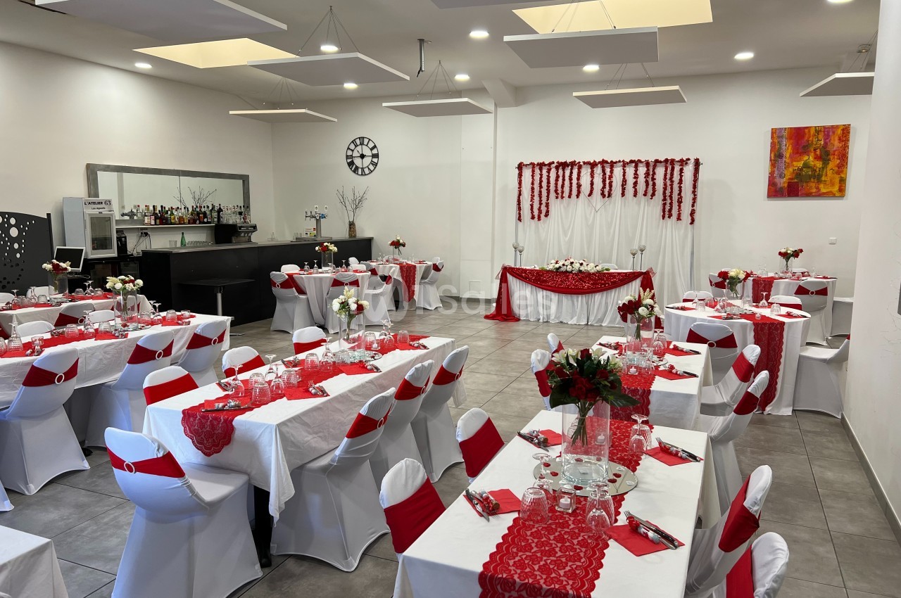 Salle de réception décorée en rouge et blanc avec tables dressées, chaises houssées et un espace pour le buffet.