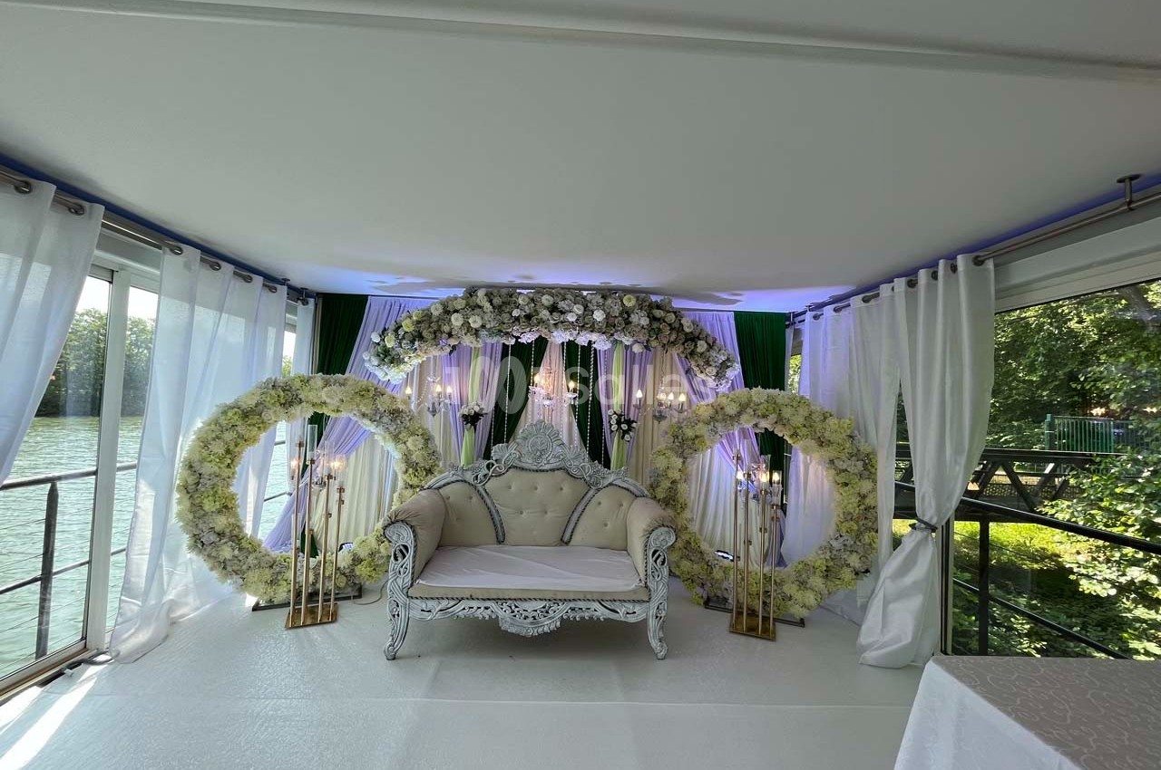 Canapé blanc décoratif entouré d'arcs floraux et de rideaux blancs dans un espace lumineux avec vue sur l'extérieur…