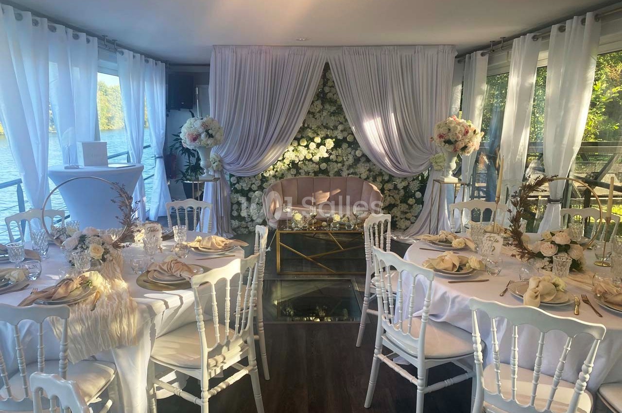 Salle décorée pour un mariage avec des tables élégantes, des chaises blanches, des fleurs et une arche florale blanche.