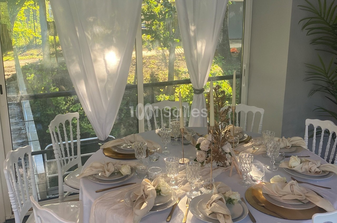 Table élégamment dressée avec nappes blanches, vaisselle raffinée, décor floral et vue sur un jardin ensoleillé.