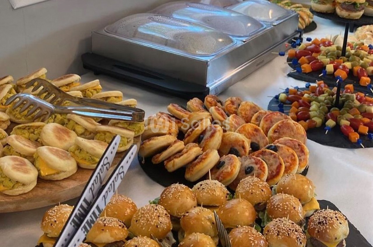Buffet varié avec mini-burgers, brochettes, muffins anglais garnis et autres amuse-bouches sur une table.