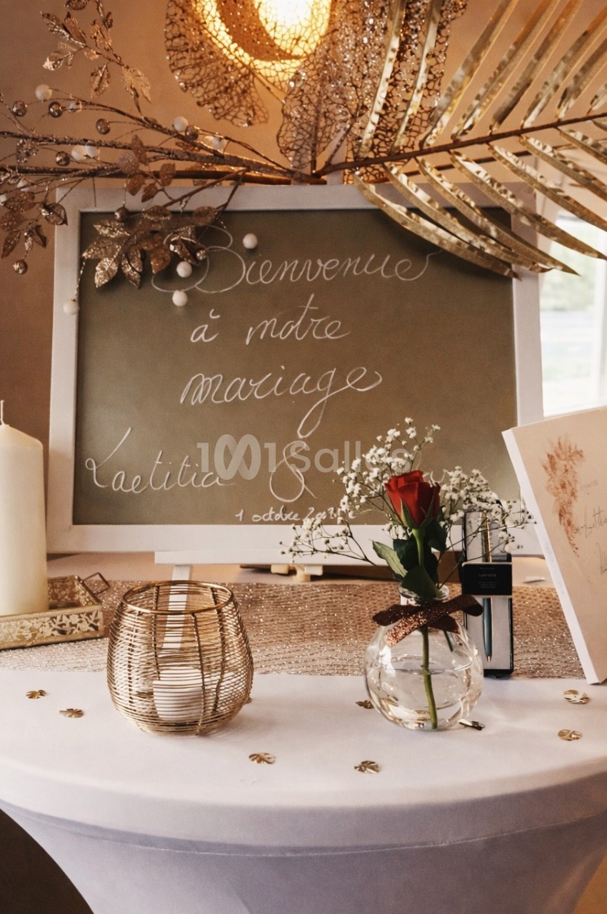 Table décorée pour un mariage avec ardoise manuscrite, bougie, rose rouge et éléments dorés.