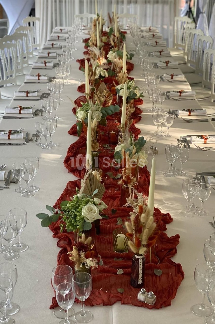 Table décorée pour un événement avec nappes blanches, chemin de table rouge, bougies et compositions florales.