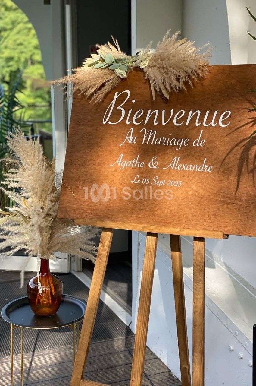 Panneau en bois sur chevalet avec message de bienvenue pour un mariage, décoré de pampas et feuillages.