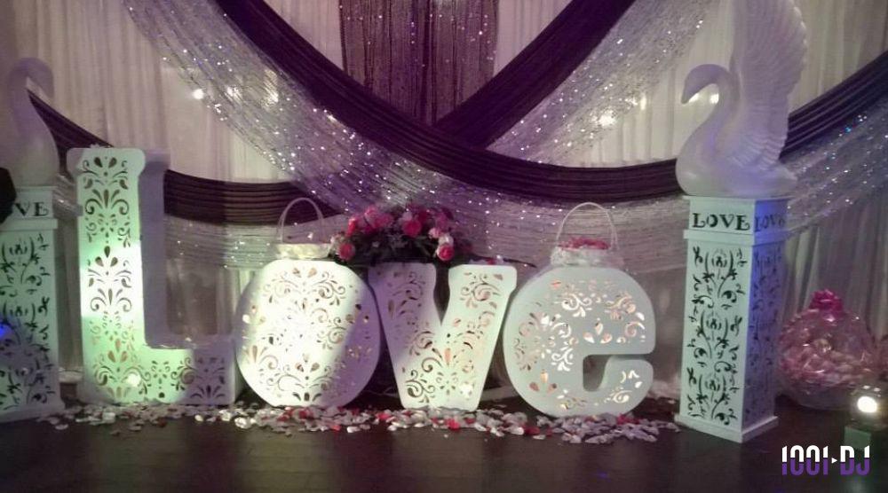 Décoration de mariage avec des lettres lumineuses formant ’LOVE’, des cygnes blancs et des pétales de fleurs au sol.