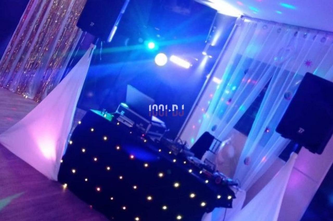 Décoration lumineuse avec une table de DJ éclairée, des rideaux scintillants et des ballons formant le chiffre 50.