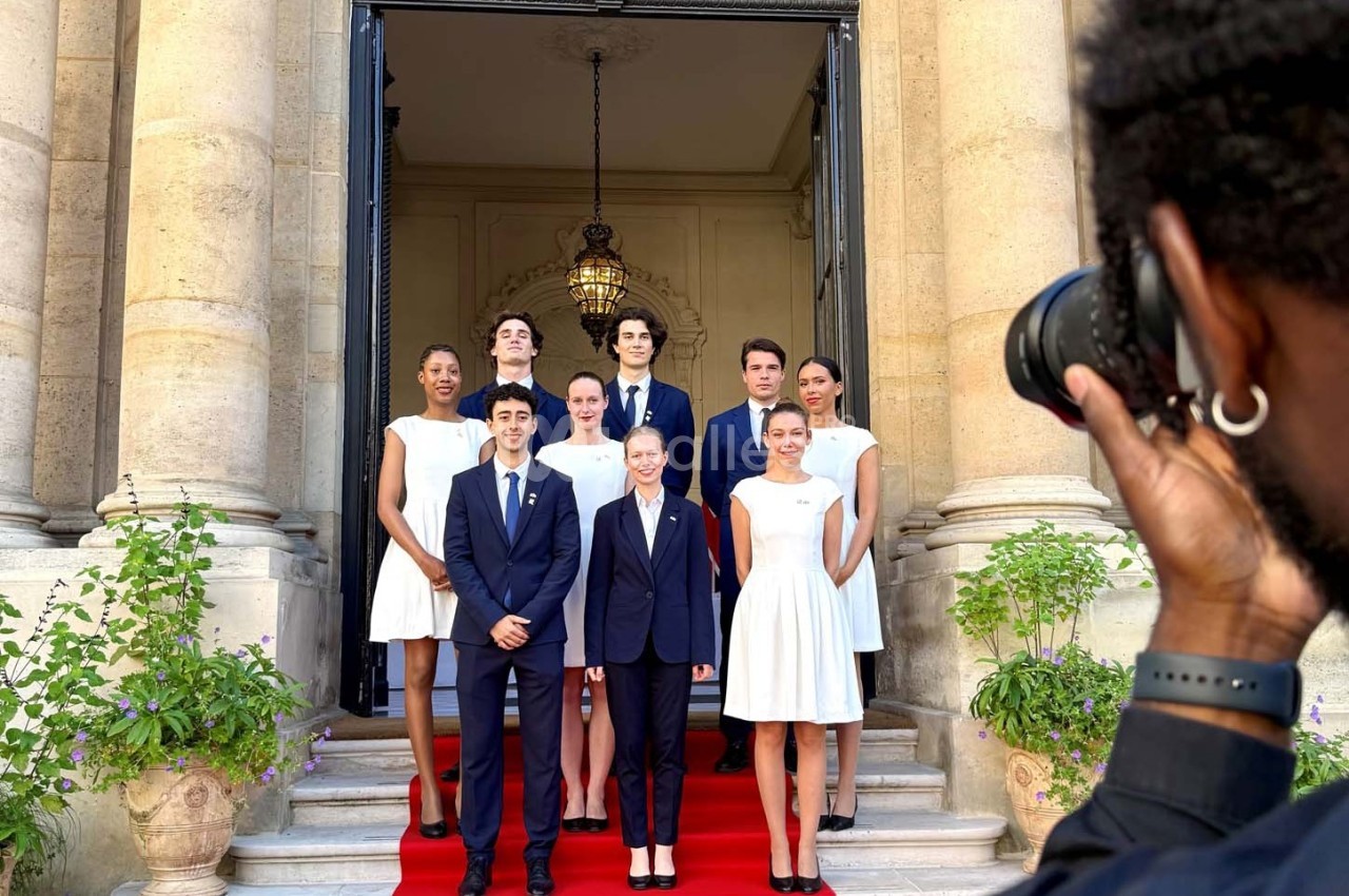 Un groupe de personnes posant sur un tapis rouge devant une entrée monumentale, photographié par un photographe.