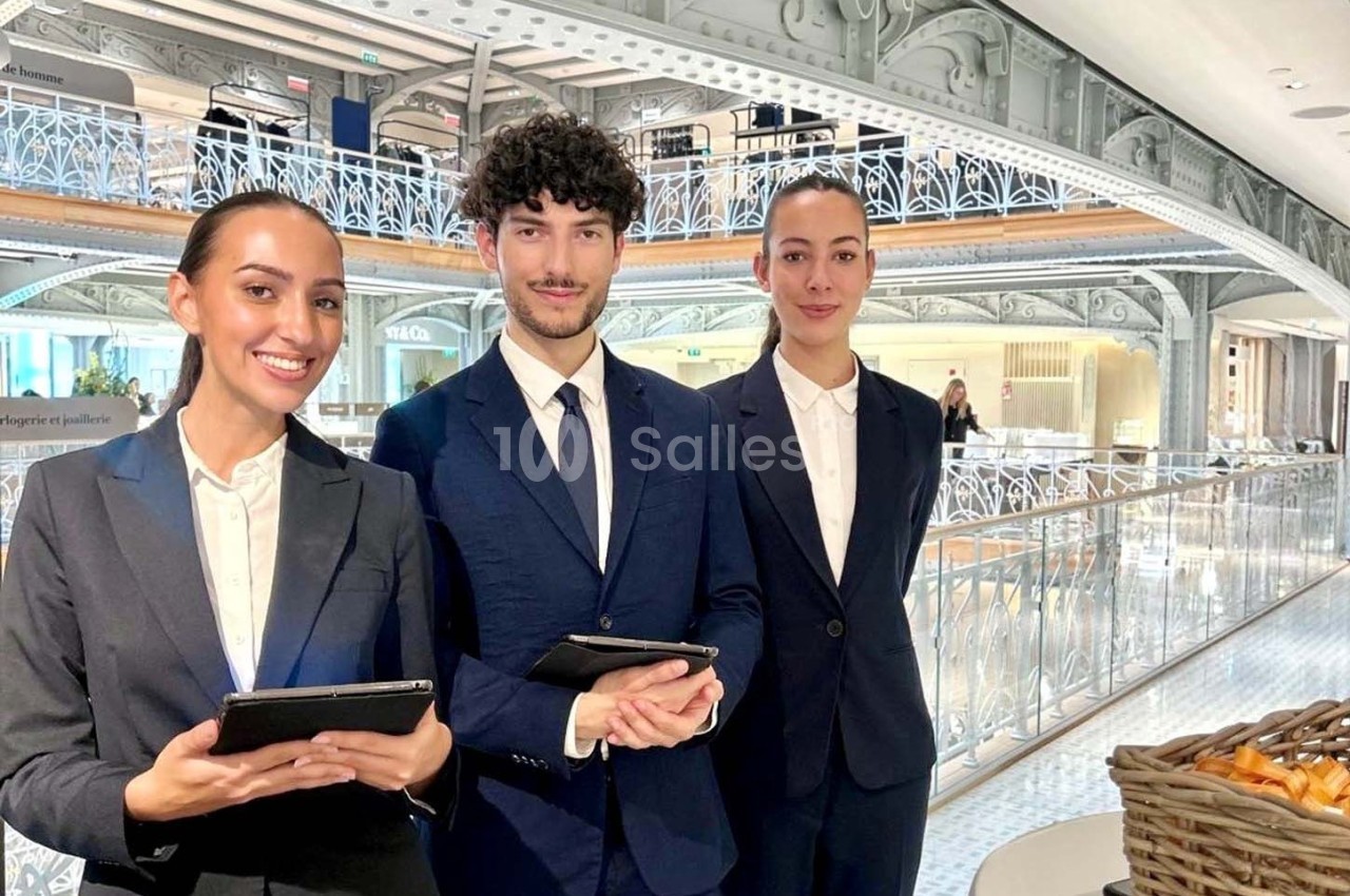 Trois personnes en costume professionnel tenant des tablettes, debout dans un espace intérieur lumineux et moderne.