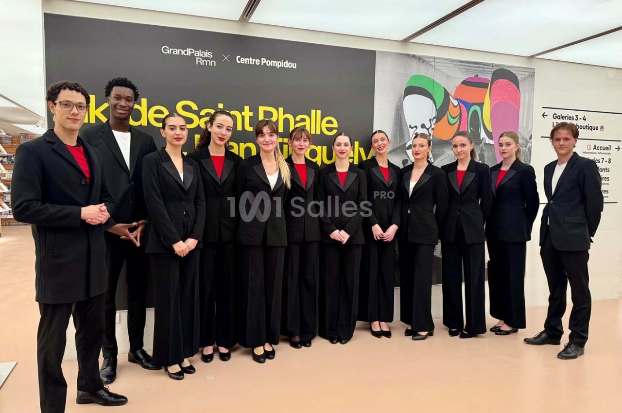 Un groupe de personnes en tenue formelle pose devant un mur affichant une exposition au Grand Palais Immersif.
