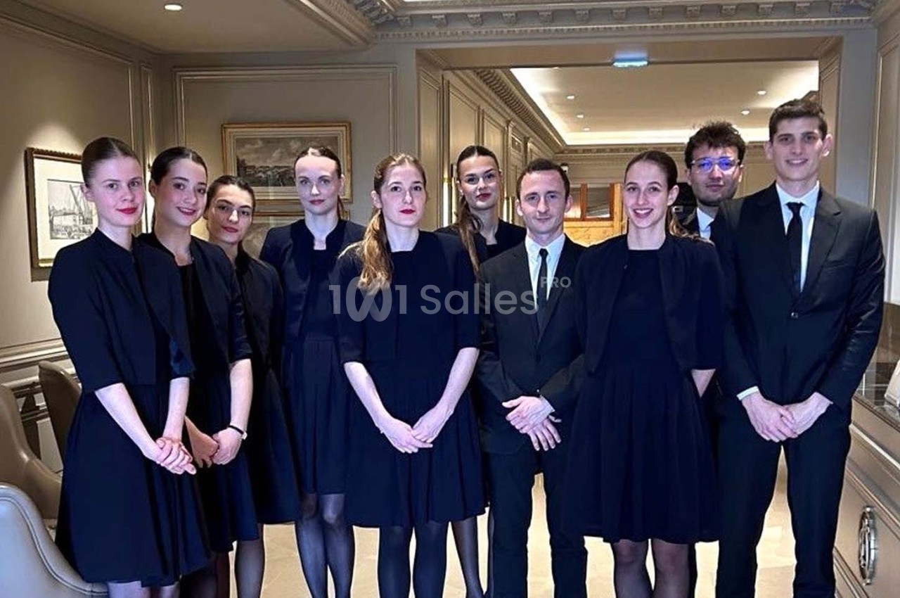 Un groupe de personnes en tenue formelle posant dans un intérieur élégant avec des murs ornés de cadres.