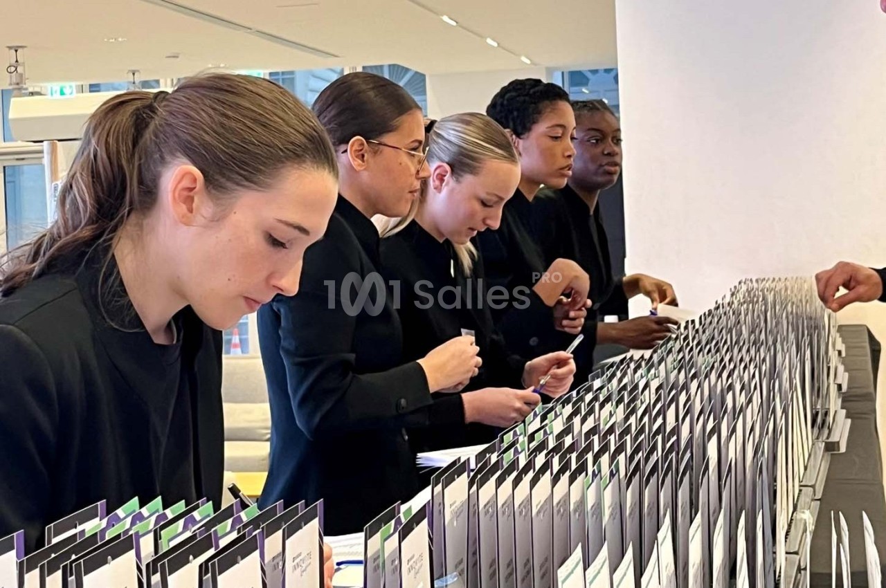 Des hôtesses en uniforme noir organisent et distribuent des badges sur une table lors d'un événement.