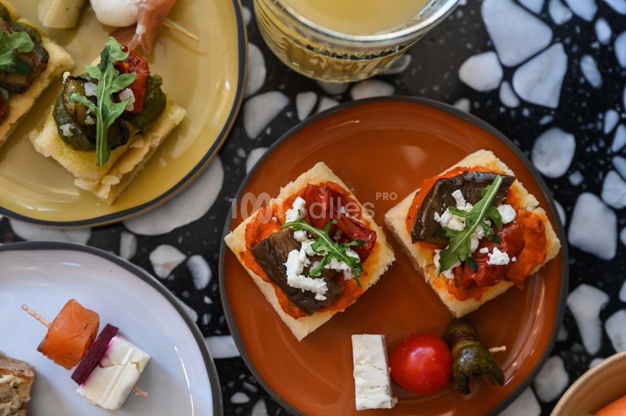 Assortiment de bouchées apéritives sur assiettes, avec légumes grillés, fromage et garnitures variées.