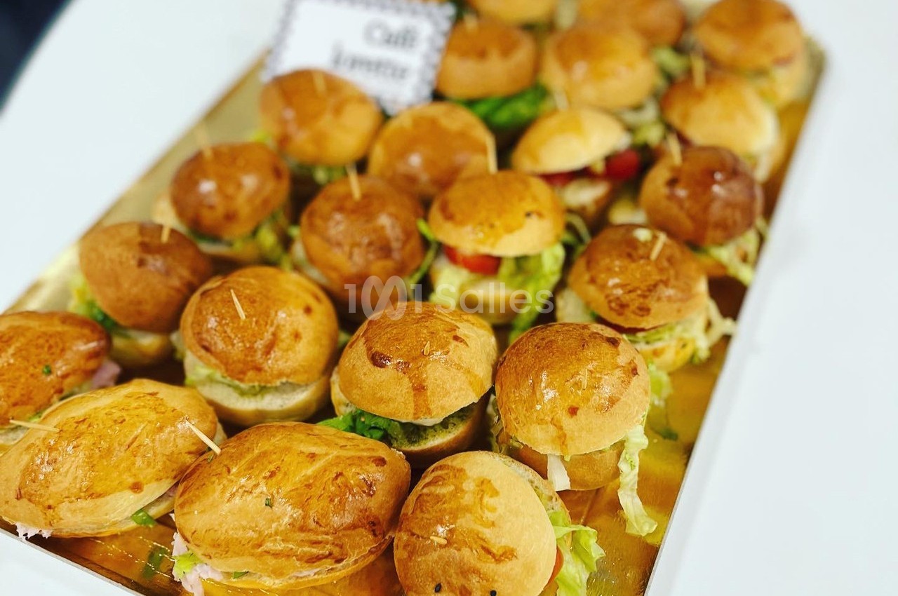 Plateau de mini-burgers garnis de salade, fromage et légumes, présentés sur un support doré.