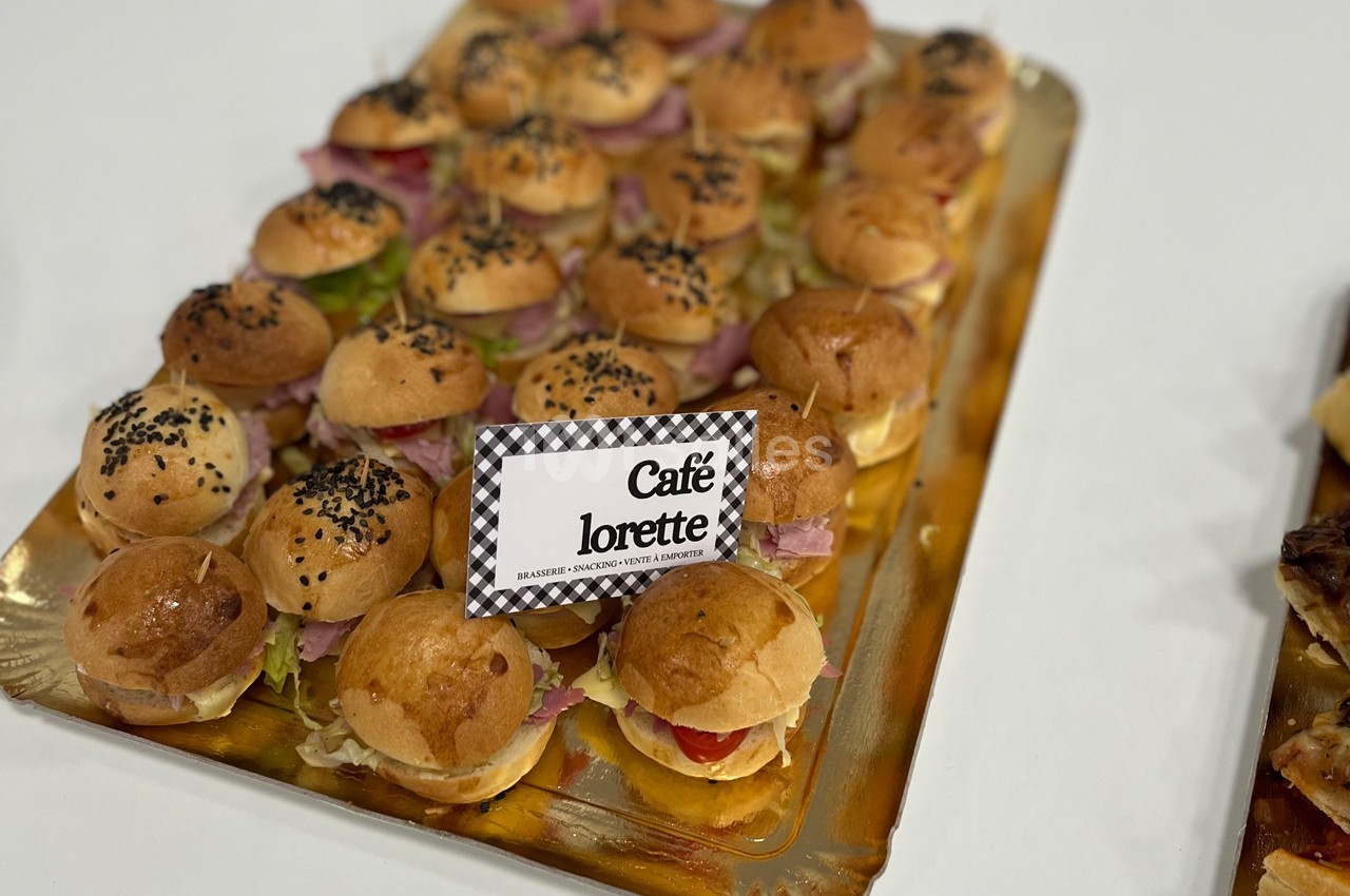 Plateaux de mini-burgers garnis de légumes et charcuterie, présentés sur une table avec une étiquette ’Café Lorette’.