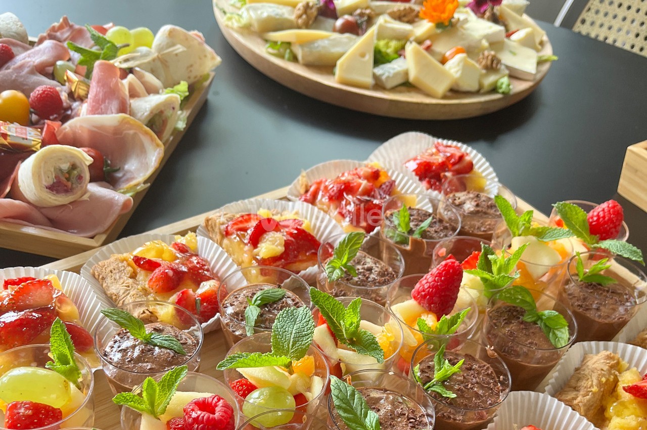Plateaux de desserts variés avec fruits frais et verrines, accompagnés de charcuteries et fromages en arrière-plan.
