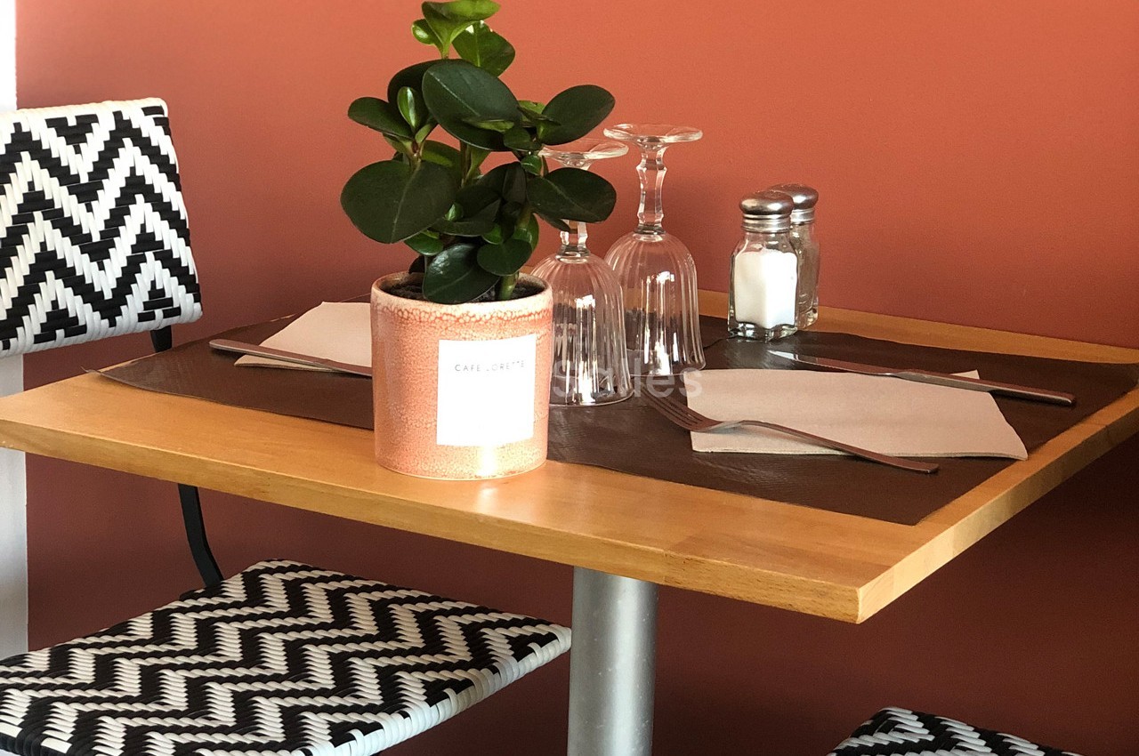 Table en bois avec deux chaises à motifs noirs et blancs, une plante en pot, des verres et des serviettes.