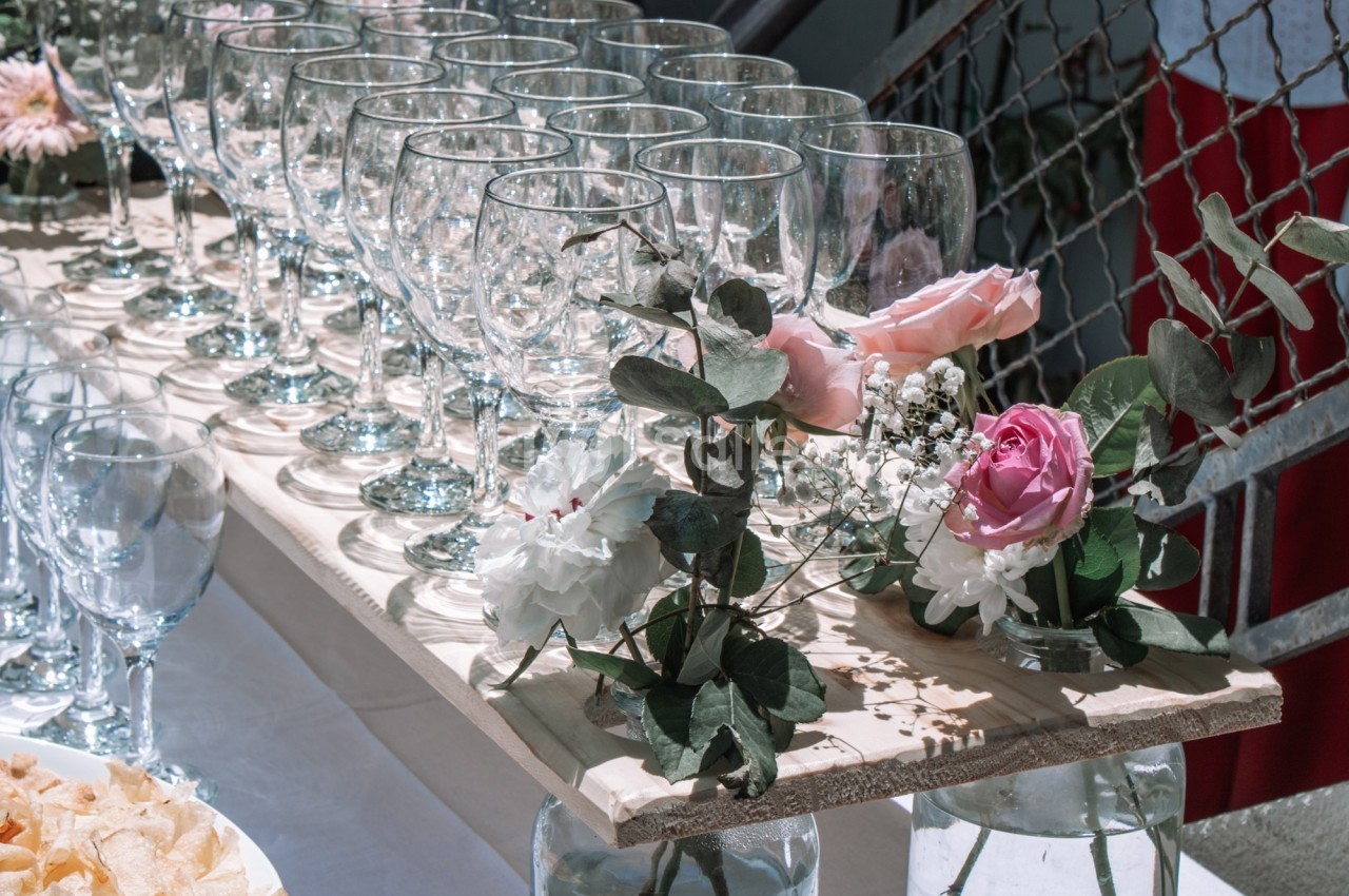 Rangée de verres à pied sur une table en bois décorée de fleurs roses et blanches.
