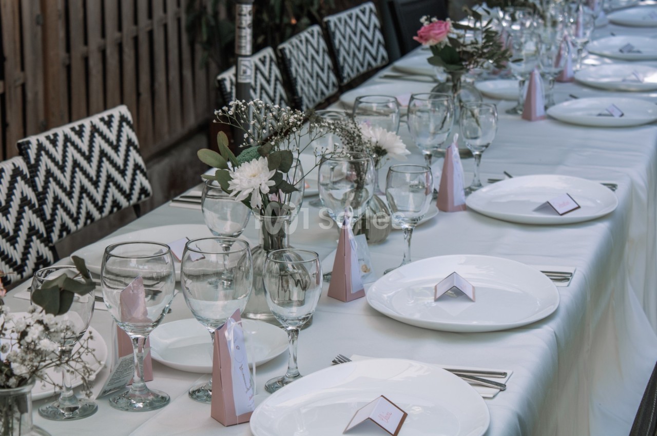 Table dressée avec nappes blanches, assiettes, verres, couverts et décorations florales pour un repas formel.