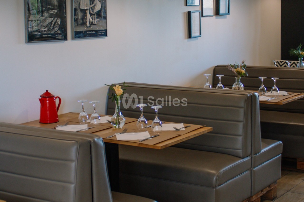 Banquettes grises avec tables dressées, verres et serviettes, dans un restaurant à la décoration sobre.