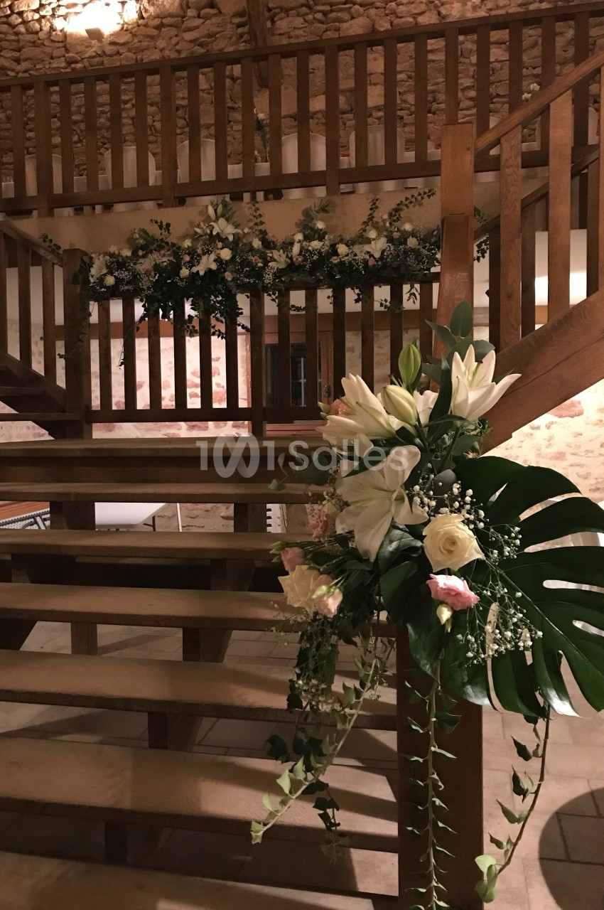 Escalier en bois décoré de fleurs blanches et roses avec feuillage, dans une salle aux murs en pierre apparente.